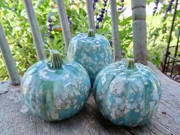 Three turquoise crystalline-glazed ceramic pumpkins on a wood surface